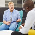 Portrait of masculine woman sharing mental health issues with African-American psychologist in  therapy session or support group, copy space